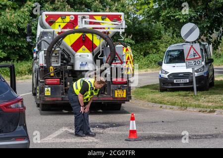 Un agente investigativo della polizia contro le collisioni che ispeziona la superficie stradale e. segni sulla scena di una collisione stradale Foto Stock