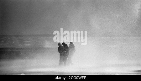 AJAXNETPHOTO. 1975. SOUTHSEA, INGHILTERRA. - TEMPESTE AUTUNNALI - TRE GIOVANI INVADITI DA ONDE TEMPESTE CHE SI INFRANGONO SUL FRONTE MARE LUNGO CLARENCE ESPLANADE. PHOTO:JONATHAN EASTLAND/AJAX REF:7526093 35 11 Foto Stock