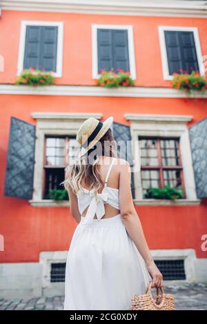 Giovane donna che cammina indossando abiti eleganti e accessori nella città vecchia di Lviv. Cappello di paglia e borsetta alla moda Foto Stock