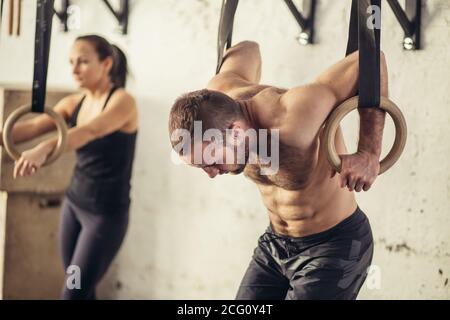 Fitness uomo bello fare immersione esercizio utilizzando anelli in palestra Foto Stock