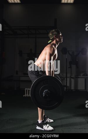 Montare il giovane uomo il sollevamento barbells cercando focalizzata, lavorando in una palestra Foto Stock