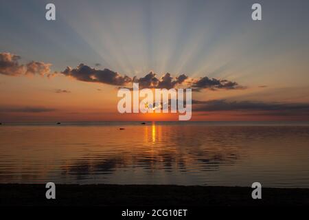 Sole con raggi nel cielo dietro le nuvole durante l'alba sopra mare Foto Stock