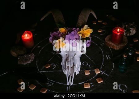 Gabbiano di capra bianco con corna, fiori, libro aperto vecchio, candele sul tavolo delle streghe. Concetto occulto, esoterico, divinazione e wicca. Halloween, giorno della dea Foto Stock