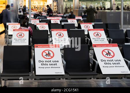 Posti a sedere bloccati con cartelli per mantenere la distanza sociale per la salute pubblica, terminal 3 dell'aeroporto di Heathrow, per la pandemia di Coronavirus Covid-19 Foto Stock