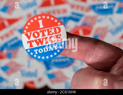 Dito con ho votato due volte pulsante davanti a molti Adesivi dati agli elettori americani alle elezioni presidenziali per illustrare vota la frode Foto Stock
