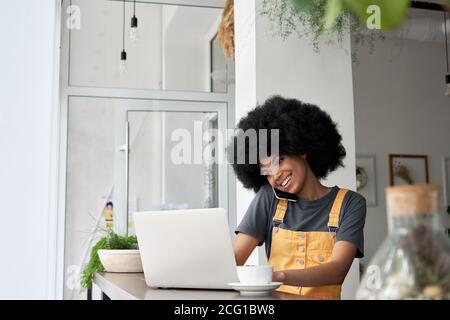 Felice giovane donna afroamericana che parla al telefono usando il laptop nel caffè. Foto Stock