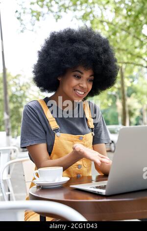 Donna africana che usa il computer che parla con un amico tramite videochiamata in un caffè all'aperto. Foto Stock