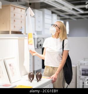 Nuova normalità durante l'epidemia di covidio. Donna caucasica shopping al dettaglio mobili e negozio di accessori per la casa indossando maschera medica protettiva per il viso Foto Stock