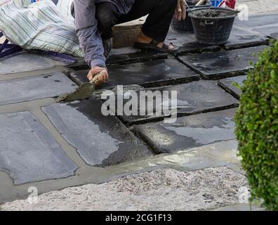 I lavoratori edili stanno pavimentando la pietra del marciapiede con cemento. Foto Stock