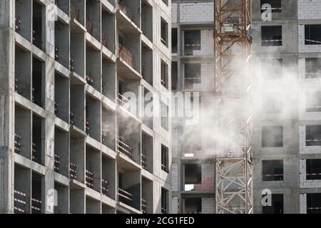 Vista della facciata di un edificio monolitico in cemento a più piani in costruzione. Recinzioni e strutture metalliche sui pavimenti. La polvere di cemento sta volando Foto Stock