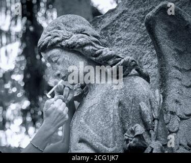 Una vista ravvicinata di una donna che illumina una sigaretta per un angelo cimitero statua Foto Stock