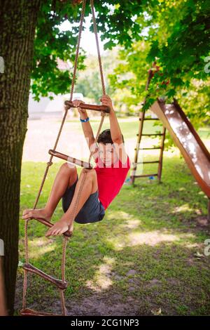 Un bel ragazzo caucasico su una scala di legno per bambini nel parco. Un giorno in natura Foto Stock