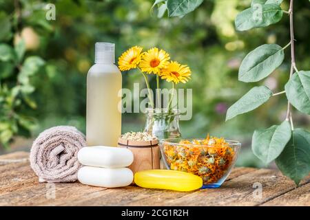 Prodotti per il benessere e gli accessori. Asciugamani, sapone e la bottiglia di plastica con estratto di calendula, calendula fiori in un pallone di vetro e la ciotola di legno con Fiore secco Foto Stock