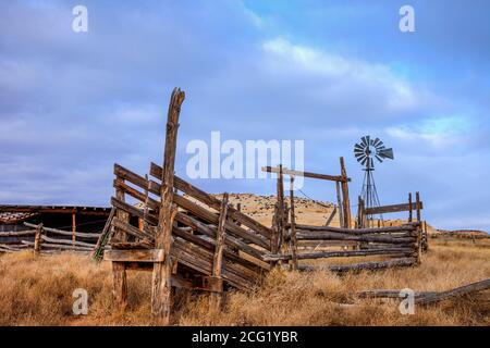 Un mulino a vento dietro un vecchio palo di legno recinto bestiame Corral e scivolo di carico nel sud-est dello Utah. Foto Stock