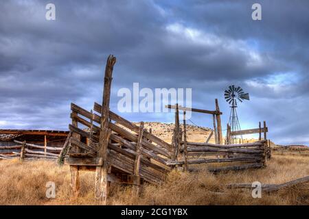 Un mulino a vento dietro un vecchio palo di legno recinto bestiame Corral e scivolo di carico nel sud-est dello Utah. Foto Stock