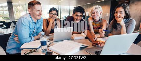 Gruppo multietnico di giovani che studiano insieme a un tavolo guardando il laptop. I giovani studenti in collaborazione con la loro scuola di assegnazione. Foto Stock
