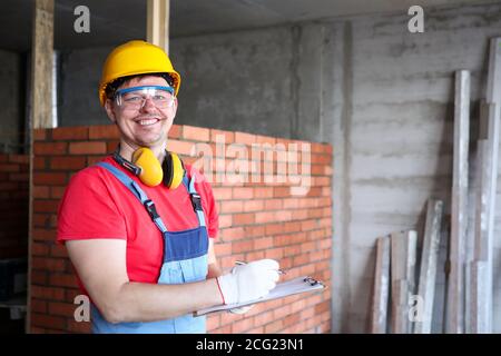 Sorridente builder scrivere sui risultati di lavoro degli appunti Foto Stock