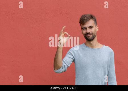 Ritratto di felice uomo soddisfatto che mostra un gesto corretto sullo spazio di copia su sfondo rosso parete. Linguaggio del corpo tutto OK. Concetto di emozione positiva Foto Stock
