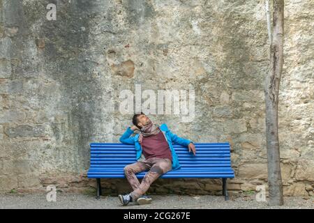 Giovane e romantico bell'uomo seduto da solo sulla panchina di fronte antico muro di pietra fortezza e in attesa di datazione Foto Stock