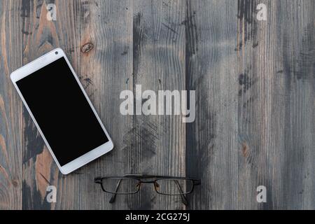 Smartphone mobile con schermo nero e vecchi occhiali su sfondo in legno vintage. Disposizione piatta, spazio di copia Foto Stock