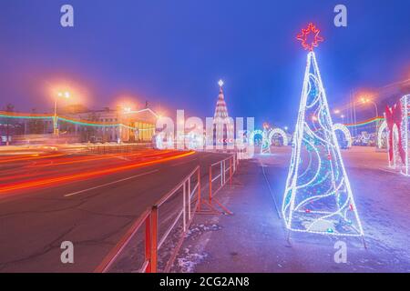 Vista sulla città del Teatro e il principale albero di Natale della città la sera la città in piena illuminazione notturna. Belle tracce di fari di automobili sulla strada Foto Stock