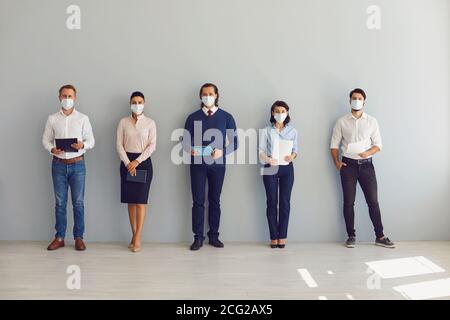 Cercatori di lavoro in maschere di faccia in attesa di colloquio di lavoro in piedi in corridoio mantenendo la distanza di sicurezza Foto Stock