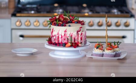 Grande bella torta di velluto rosso, con fiori e bacche in cima. Deliziosi muffin dolci con crema, decorati con fragole e mirtilli. Foto Stock