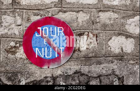 Parcheggio vietato simbolo giorno e notte (francese: Jour et Nuit). Un cerchio rosso e blu su un muro di pietra. Foto Stock