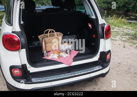 Pacchetto picnic e cestino con croissant e panini si trovano nel bagagliaio dell'auto da berlina. Weekend all'aperto, viaggi locali Foto Stock