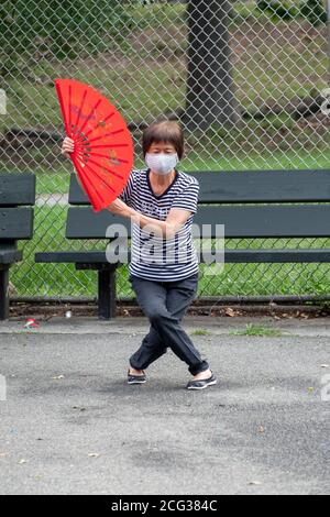 Il leader di una classe Tai Chi che utilizza ventilatori rossi pieghevoli. In un parco a Flushing, Queens, New York City. Foto Stock