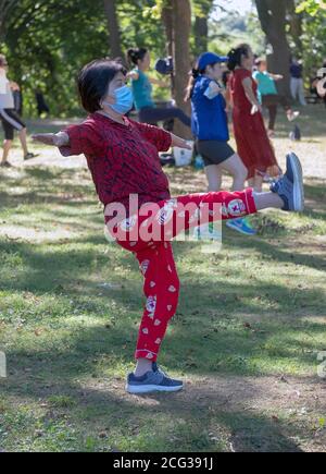 Una donna asiatica americana di mezza età in una classe di danza all'aperto è una delle poche che indossa una maschera. In un parco a Queens, New York Foto Stock
