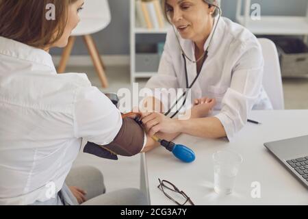 Medico maturo che misura la pressione sanguigna del paziente in clinica. Cardiologo aiutare donna con ipertensione in ospedale Foto Stock