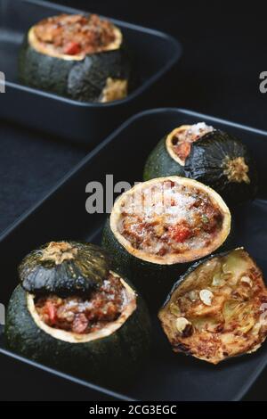 Zucchine rotonde farcite con carne, pomodori e parmigiano su piatti scuri. Sfondo scuro. Foto Stock