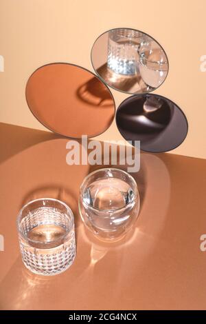 Due bicchieri d'acqua con ombre accanto a specchi rotondi Foto Stock