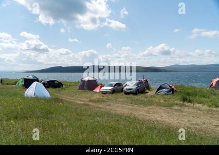 La gente si rilassa in un campo tenda sulla riva di un grande lago in estate. Foto Stock