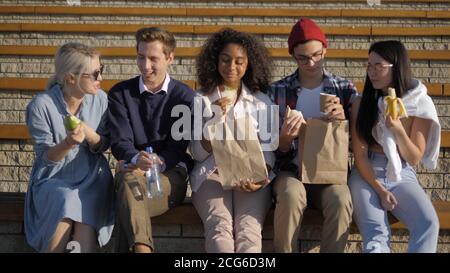 Gruppo di studenti affamati che pranzano seduti sulle scale. Foto Stock