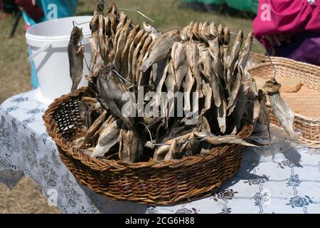 La pesca di pesce salato e secco, strung su un filo, giace in un cestino di wicker salice in piedi sulla tavola. Foto Stock