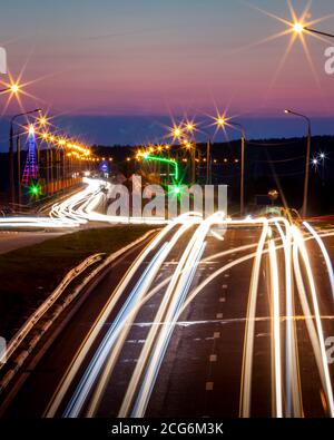 Tracce di fari da auto che si muovono di notte sul ponte, illuminati da lanterne. Paesaggio astratto della città con autostrada. Foto Stock