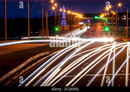Tracce di fari da auto che si muovono di notte sul ponte, illuminati da lanterne. Paesaggio astratto della città con autostrada. Foto Stock