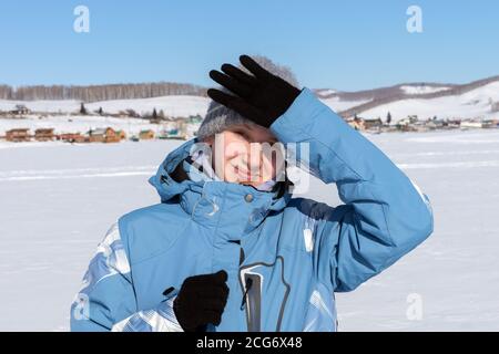 Una giovane sciatrice è bloccata da una mano dal sole, si erge su un lago ghiacciato e neve sullo sfondo del paese. Foto Stock