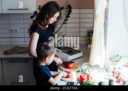 Bella mamma e figlio tagliato verdure fresche per insalata con un coltello Foto Stock