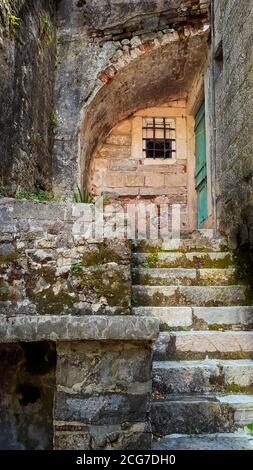 Antica scalinata in pietra ricoperta di muschio che conduce alla vecchia porta in legno turchese e alla finestra con griglia nella vecchia città di Cattaro, Montenegro, Europa. Foto Stock