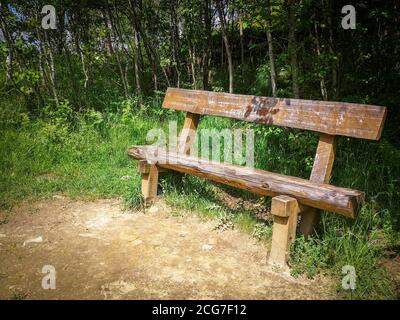 Vista frontale di una panca vuota in legno in un parco verde solitario su un parco collinare vicino ai monti Carpazi. Giorno di sole, cielo blu. Foto Stock