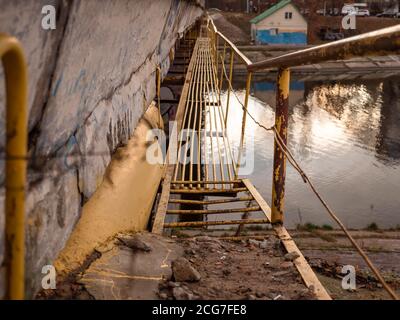 Stretto ponte tecnico con barre metalliche per la manutenzione di un grande ponte di cemento sul canale d'acqua. Due sponde del canale. Foto Stock