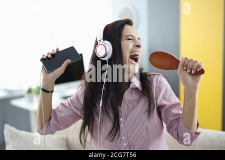 Donna con le cuffie e pettinare in mano canta emotivamente Foto Stock