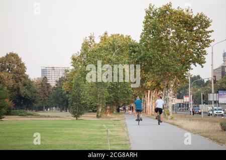 BELGRADO, SERBIA - 21 AGOSTO 2018: Due ciclisti in bicicletta che attraversano un parco su una pista ciclabile nel moderno quartiere di Belgrado, chiamato No Foto Stock