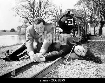 L'agente speciale John Steed (Patrick Macnee) è lì appena in tempo per salvare il bel collo di Emma Peel (Diana Rigg) in una scena in fase di ripresa per la nuova serie di 'The Avengers'. La posizione era la ferrovia in miniatura nella tenuta di Lord Gretton's Stapleford Park. Foto Stock