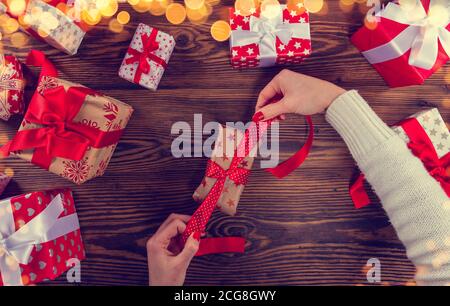 Dettaglio delle mani della donna che imballano i regali di Natale. Concetto di festa e festa. Colore con design a filtro retrò. Immagine ad alta risoluzione Foto Stock