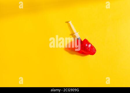 Sirina monouso in plastica con sangue o vaccino in un bicchiere rosso su sfondo giallo con ombra, spazio copia. Halloween Foto Stock