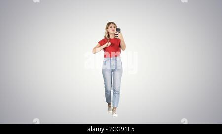 Bionda passeggiate e preening cercando nel telefono sul gradiente dello sfondo. Foto Stock